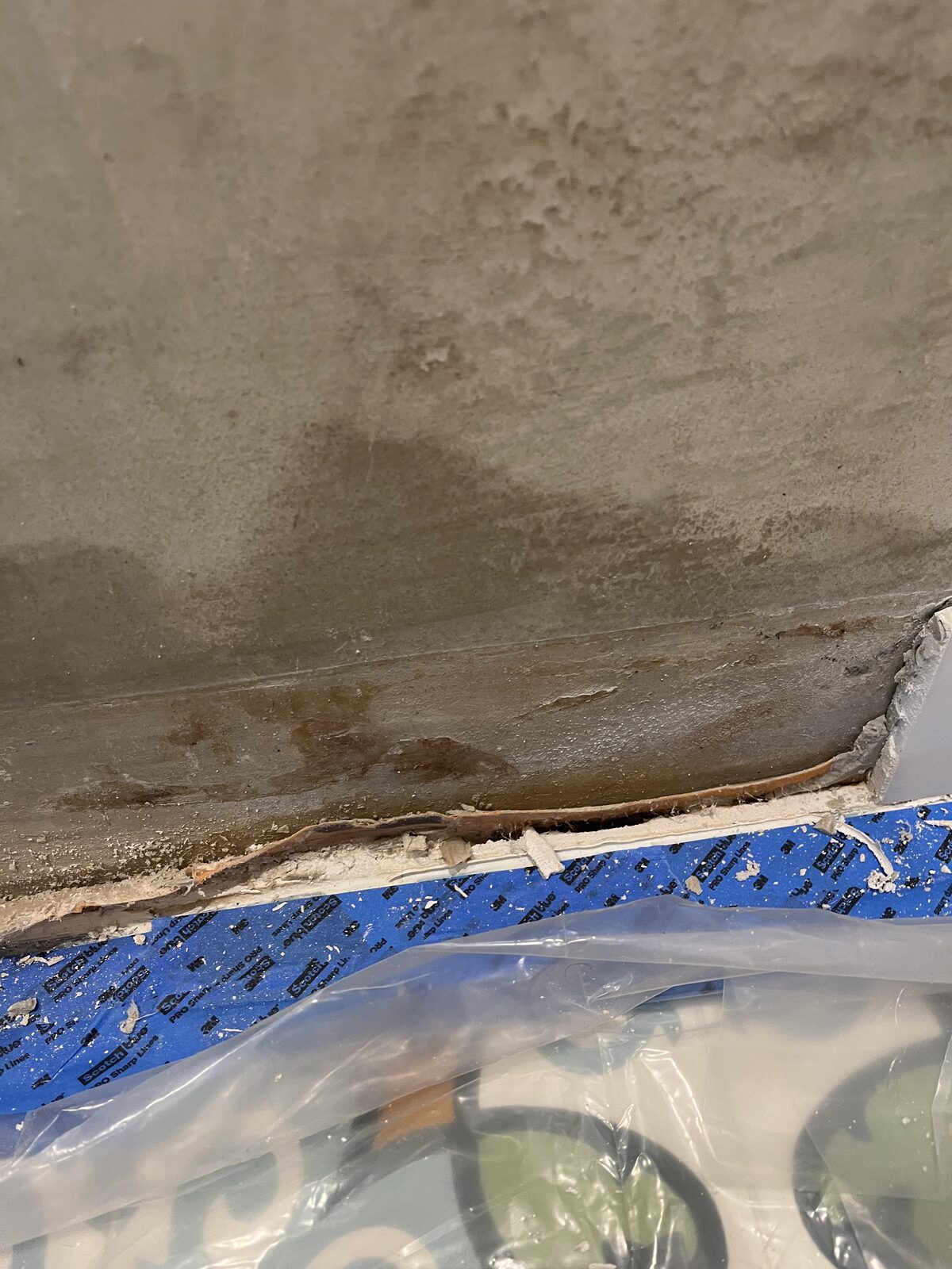 Rust and water damage bleeding through the substrate at the base of a bathroom wall — hidden failure from poor installation